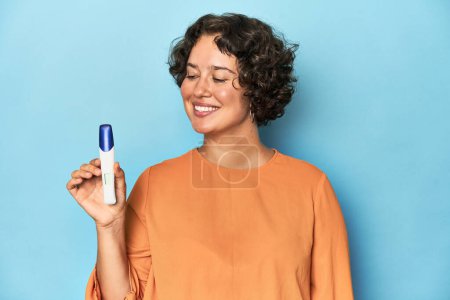 Téléchargez les photos : Jeune femme caucasienne tenant un test de grossesse, studio fond bleu. - en image libre de droit