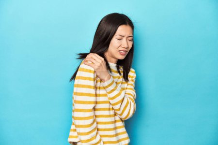 Téléchargez les photos : Femme asiatique en pull jaune rayé, ayant une douleur à l'épaule. - en image libre de droit