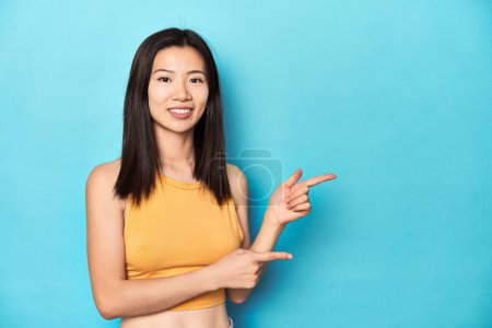 Téléchargez les photos : Femme asiatique en haut jaune d'été, installation du studio, excité pointant avec les index loin. - en image libre de droit