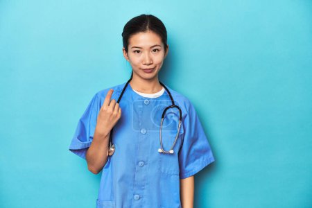 Téléchargez les photos : Infirmière asiatique avec stéthoscope, studio médical tourné, pointant du doigt vers vous comme si inviter se rapprocher. - en image libre de droit