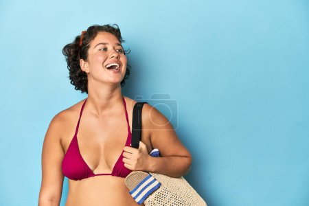 Photo for Young Caucasian woman in bikini holding a beach bag, studio shot. - Royalty Free Image