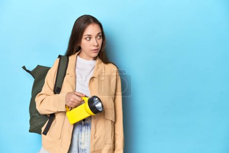Téléchargez les photos : Femme voyageuse illuminant avec une lampe de poche sur fond bleu. - en image libre de droit