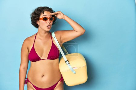 Photo for Young Caucasian woman in bikini holding a beach cooler, studio shot. - Royalty Free Image
