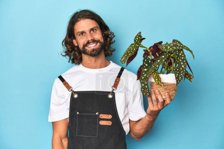 Foto de Jardinero de pelo largo con barba sosteniendo una planta feliz, sonriente y alegre. - Imagen libre de derechos