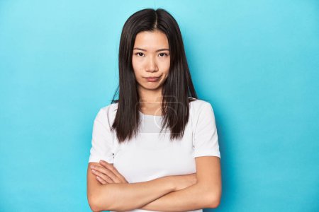 Foto de Mujer asiática joven en camiseta blanca, toma de estudio, mirada infeliz en la cámara con expresión sarcástica. - Imagen libre de derechos