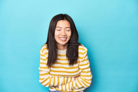 Foto de Mujer asiática en suéter amarillo rayado, riendo y divirtiéndose. - Imagen libre de derechos