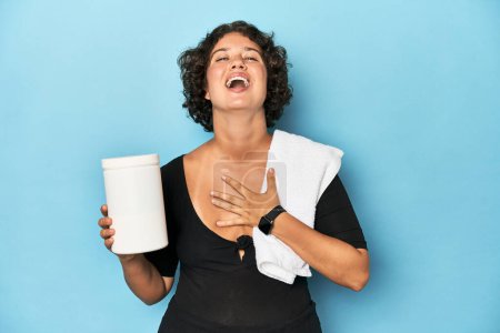 Photo for Young sportswoman with protein shake laughs out loudly keeping hand on chest. - Royalty Free Image