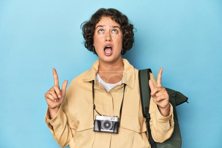 Téléchargez les photos : Jeune voyageuse avec caméra vintage pointant à l'envers avec bouche ouverte. - en image libre de droit