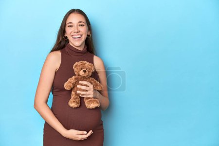Photo for Pregnant woman holding a plush baby toy on a blue studio. - Royalty Free Image