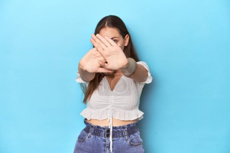 Téléchargez les photos : Jeune femme élégante en chemisier blanc sur fond de studio bleu faisant un geste de déni - en image libre de droit