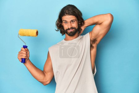 Photo for Bearded man painting with a yellow roller touching back of head, thinking and making a choice. - Royalty Free Image