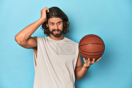 Photo for Bearded man with basketball in blue studio being shocked, she has remembered important meeting. - Royalty Free Image