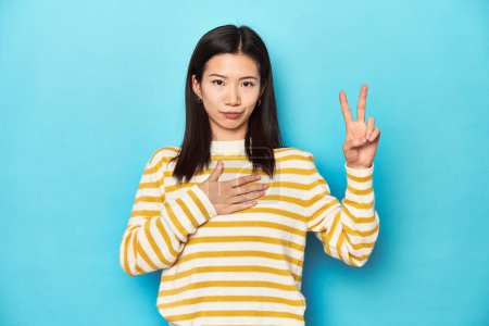 Photo for Asian woman in striped yellow sweater, taking an oath, putting hand on chest. - Royalty Free Image