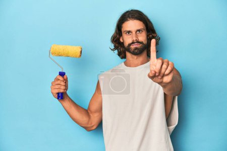 Photo for Bearded man painting with a yellow roller showing number one with finger. - Royalty Free Image