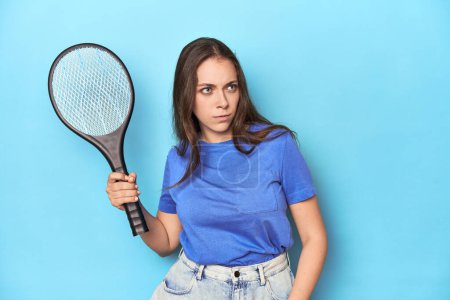 Photo for Woman holding an electric mosquito zapper in a blue studio. - Royalty Free Image