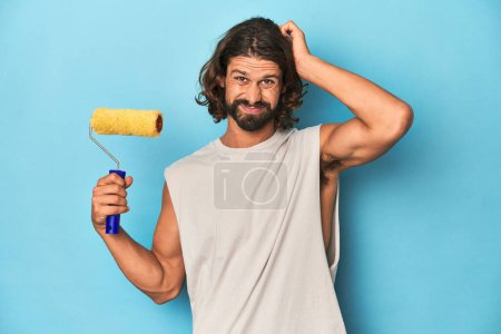 Photo for Bearded man painting with a yellow roller being shocked, she has remembered important meeting. - Royalty Free Image