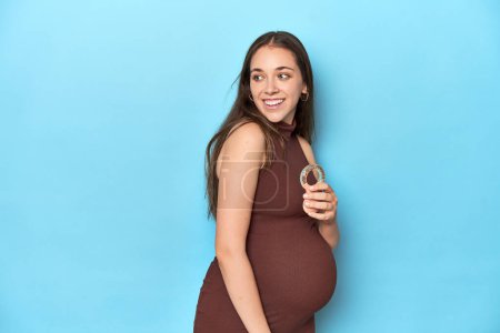Téléchargez les photos : Attendre une femme tenant une lanière de bébé dans un studio bleu. - en image libre de droit
