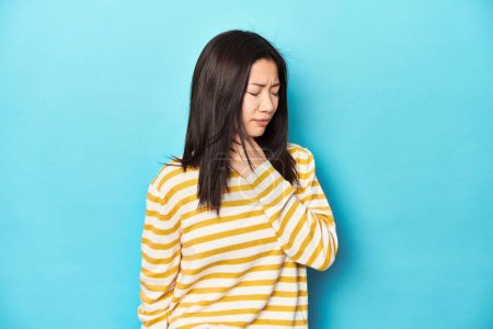 Foto de Mujer asiática en suéter amarillo rayado, sufre dolor de garganta debido a un virus o infección. - Imagen libre de derechos
