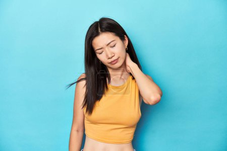 Téléchargez les photos : Femme asiatique en haut jaune d'été, installation du studio, douleur au cou due à un mode de vie sédentaire. - en image libre de droit