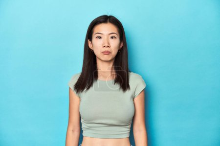 Téléchargez les photos : Femme asiatique en haut vert d'été, toile de fond studio, triste, visage sérieux, se sentant misérable et mécontent. - en image libre de droit