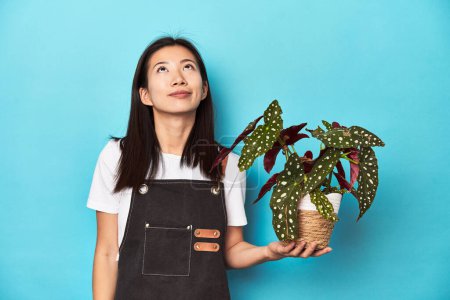 Téléchargez les photos : Jeune jardinier asiatique tenant usine, toile de fond studio, rêvant d'atteindre des objectifs et des buts - en image libre de droit