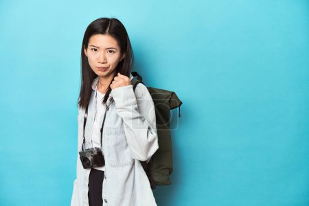 Photo for Young Asian traveler ready to capture adventures, showing fist to camera, aggressive facial expression. - Royalty Free Image