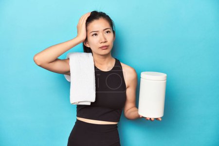 Photo for Young Asian sportswoman with protein bottle, gym setup, being shocked, she has remembered important meeting. - Royalty Free Image