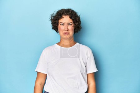 Foto de Mujer joven caucásica con el pelo corto golpea las mejillas, tiene expresión cansada. Concepto de expresión facial. - Imagen libre de derechos