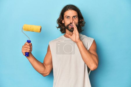 Photo for Bearded man painting with a yellow roller is saying a secret hot braking news and looking aside - Royalty Free Image