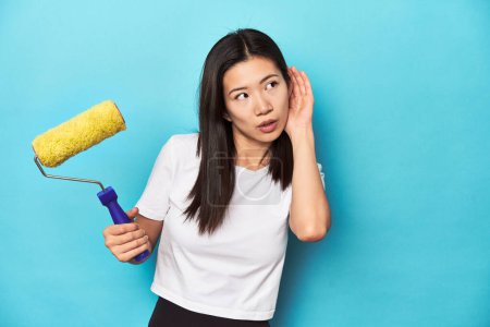 Téléchargez les photos : Jeune femme asiatique avec rouleau de peinture, concept de bricolage, en essayant d'écouter un potins. - en image libre de droit