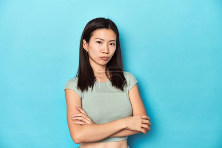 Photo for Asian woman in summer green top, studio backdrop, suspicious, uncertain, examining you. - Royalty Free Image
