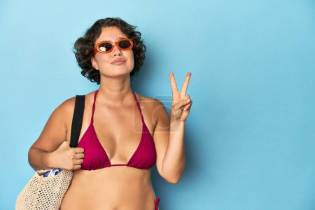 Téléchargez les photos : Jeune femme en bikini avec sac de plage montrant numéro deux avec les doigts. - en image libre de droit