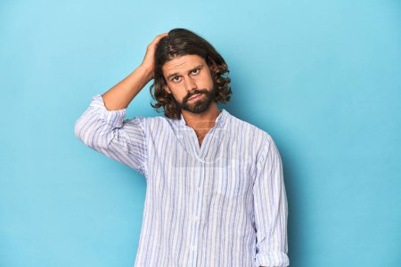Photo for Man with beard in blue striped shirt, blue studio tired and very sleepy keeping hand on head. - Royalty Free Image