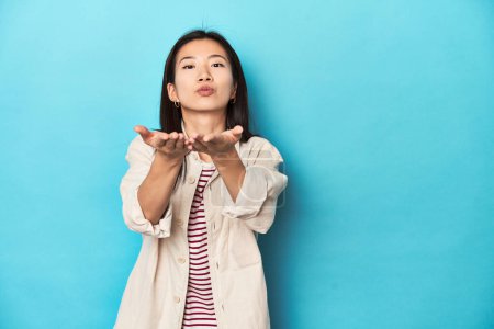 Photo for Asian woman in layered shirt and striped t-shirt, folding lips and holding palms to send air kiss. - Royalty Free Image