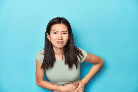 Photo for Asian woman in summer green top, studio backdrop, having a liver pain, stomach ache. - Royalty Free Image