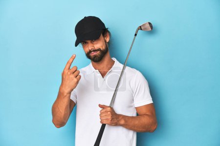Foto de Golfista de pelo largo con palo y sombrero apuntando con el dedo en usted como si invitando a acercarse. - Imagen libre de derechos