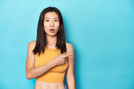 Téléchargez les photos : Femme asiatique en haut jaune d'été, installation studio, pointant vers le côté - en image libre de droit
