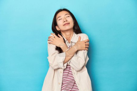 Foto de Mujer asiática con camisa en capas y camiseta a rayas, abrazos, sonriente despreocupada y feliz. - Imagen libre de derechos