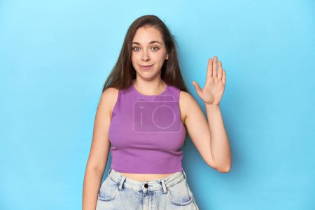 Foto de La mujer a la moda joven en la parte superior púrpura sobre el fondo azul sonriente alegre que muestra el número cinco con los dedos. - Imagen libre de derechos