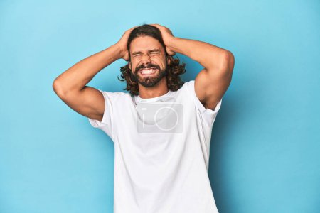 Photo for Bearded man in a white shirt, blue backdrop screaming, very excited, passionate, satisfied with something. - Royalty Free Image
