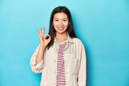 Foto de Mujer asiática con camisa en capas y camiseta a rayas, alegre y confiado mostrando gesto ok. - Imagen libre de derechos