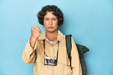 Téléchargez les photos : Jeune voyageuse avec caméra vintage montrant poing à caméra, expression faciale agressive. - en image libre de droit
