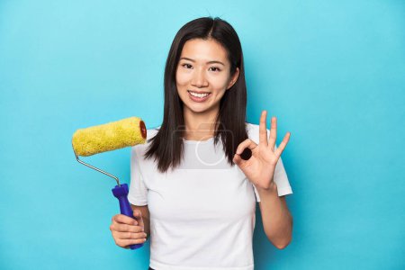 Photo for Young Asian woman with paint roller, DIY concept, cheerful and confident showing ok gesture. - Royalty Free Image