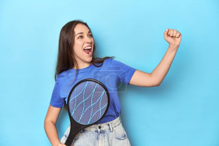 Foto de Mujer con un zapper de insecto eléctrico sobre un fondo azul levantando puño después de una victoria, concepto ganador. - Imagen libre de derechos