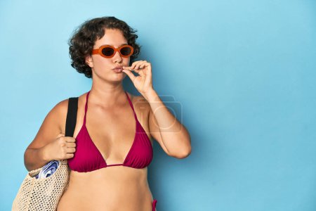 Téléchargez les photos : Jeune femme en bikini avec sac de plage avec les doigts sur les lèvres gardant un secret. - en image libre de droit