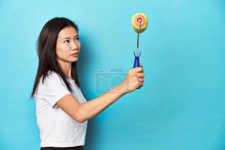 Photo for Young Asian woman with yellow paint roller, studio shot. - Royalty Free Image