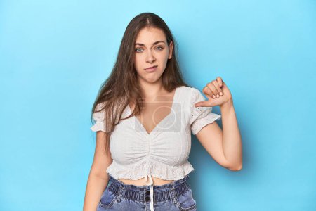 Photo for Stylish young woman in white blouse on a blue studio backdrop showing thumb down, disappointment concept. - Royalty Free Image