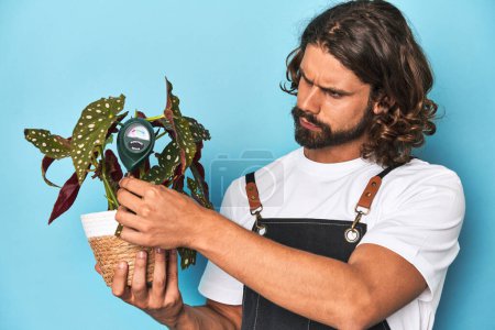 Téléchargez les photos : Jardinier barbu avec plante et humidimètre en studio bleu. - en image libre de droit