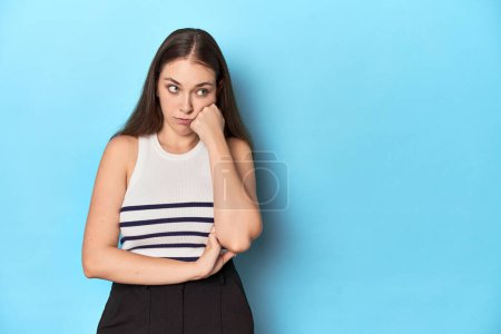 Téléchargez les photos : Femme dans un haut rayé posant sur un fond de studio bleu qui se sent triste et coûteux, en regardant l'espace de copie. - en image libre de droit