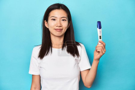 Photo for Young Asian woman holding a pregnancy test, studio shot. - Royalty Free Image